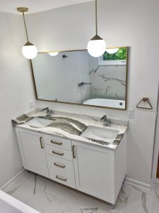 downward view of bathroom remodel with white cabinets and grey and white marbled countertops with double sinks