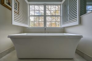 new porcelain bathtub in front of wide windows that open up in a newly remodeled bathroom